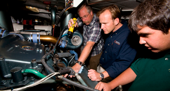 two students with instructor examine engine